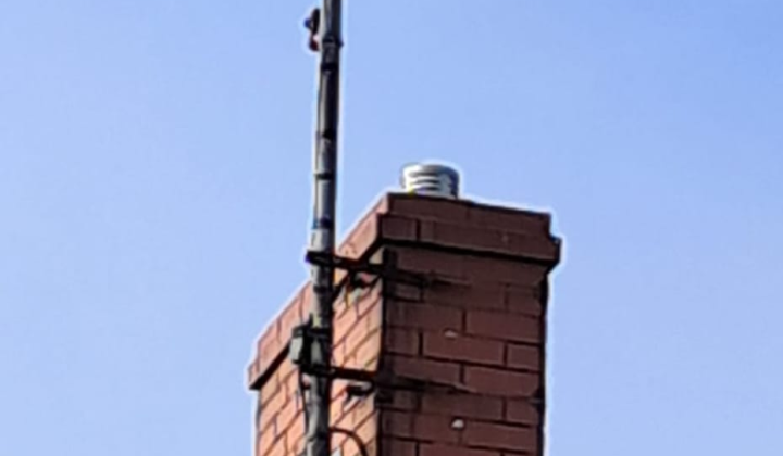 Brick chimney with an aerial and lead flashing above a tiled roof.