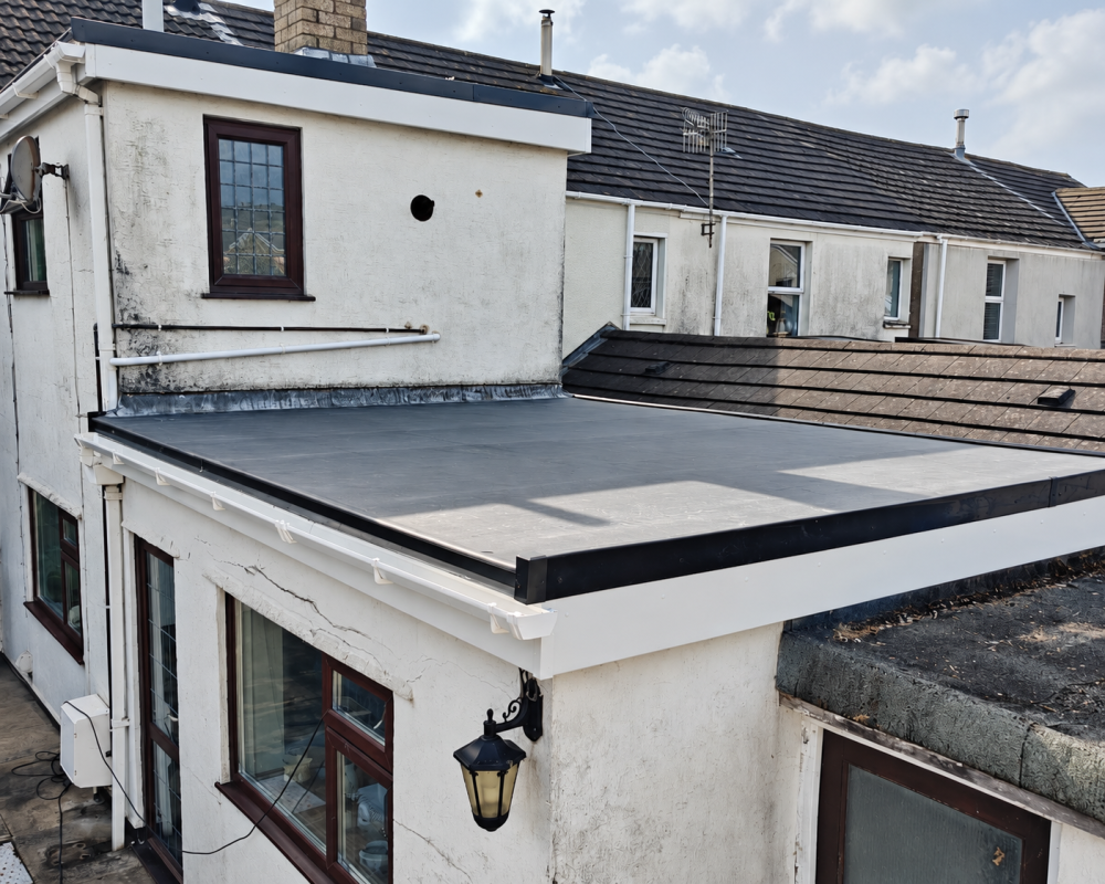 Flat roof covering on a white rendered extension, showing the roof edges and adjoining building.